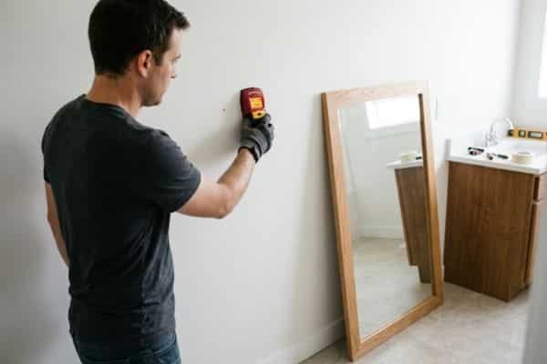 Using a stud finder on a bathroom wall before hanging a heavy framed mirror